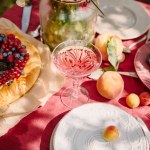 Wineglass, berries pie and fruits on table in garden with sunlight