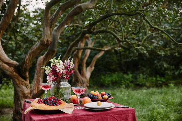 букет цветов, бокалы, фрукты и пирог на столе в саду
