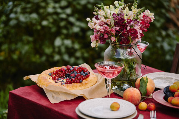 bouquet of flowers in glass jar and wineglass on table in garden