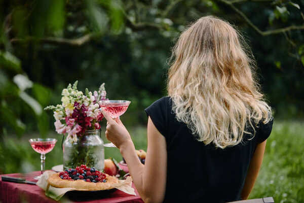 rear view of woman holding glass of wine at table in garden