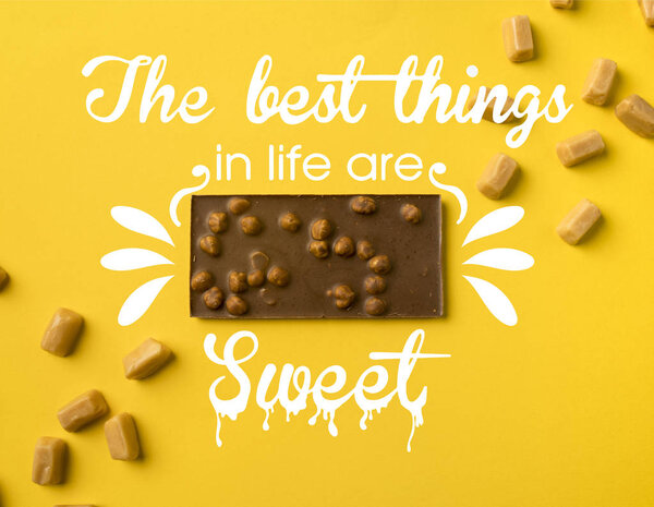 Top view of chocolate bar with scattered iris milk candies isolated on yellow with "the best things in life are sweet" lettering