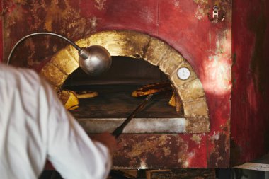 cropped shot of chef taking pizza from masonry oven at restaurant kitchen clipart
