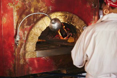 cropped shot of chef taking pizza from brick oven at restaurant kitchen clipart