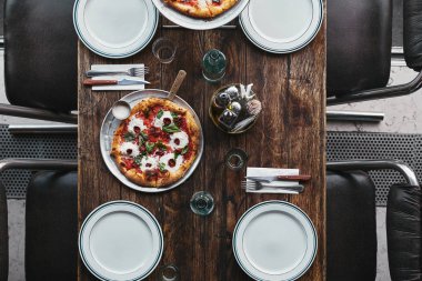 top view of tasty pizza margherita on tray and plates on rustic table at restaurant clipart