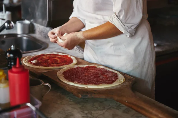 Şef peynir parçaları koyarak pizza lokanta mutfağı kadeh kırpılmış