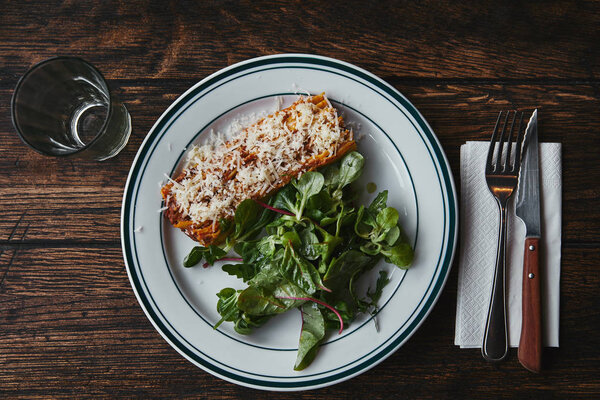 top view of delicious lasagne with green leaves on rustic wooden teable