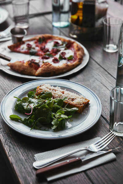 close-up shot of freshly baked pizza and lasagne on wooden table 