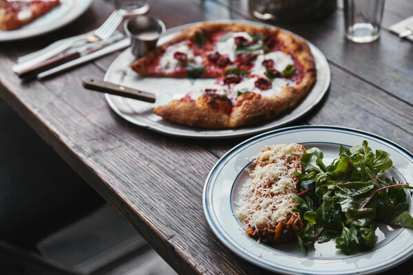 close-up shot of tasty pizza and lasagne on wooden table 