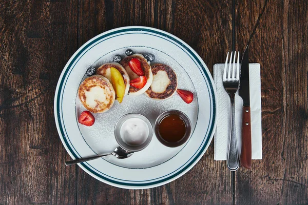 top view of cheese pancakes with bowls of dippings and cutlery on rustic wooden table