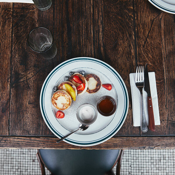 вид на вкусные творожные блинчики с чашами с макаронами и столовыми приборами на деревянном столе в ресторане
