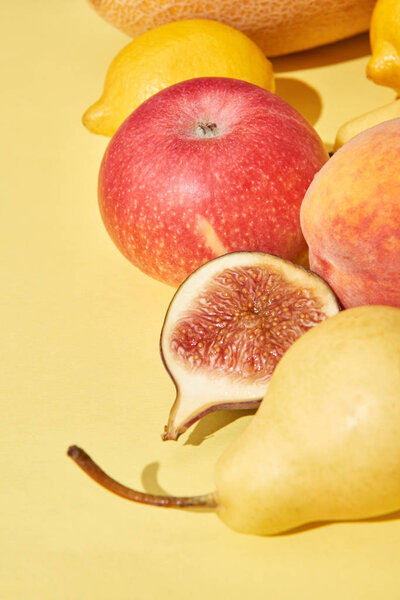 close-up view of fresh ripe pear, apple, peach, fig and lemons on yellow