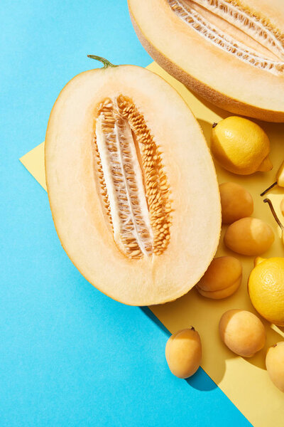 top view of ripe halved melon and fresh pears, lemons, apricots on blue and yellow background