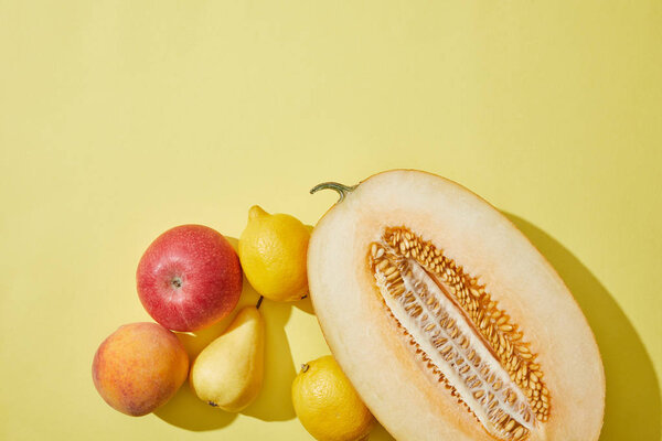 top view of halved melon, apple, peach, pear and lemons on yellow background