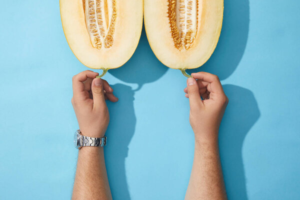 cropped shot of human hands and halved ripe melon on blue 