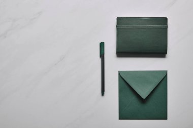 Yeşil zarf ve defter kalem üzerinde beyaz mermer zemin ile