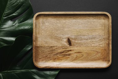 Empty wooden board on black background with monstera leaves clipart