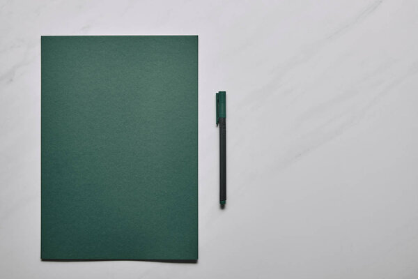 Green paper and pen on white marble background