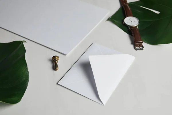 空白信封和观看在白色大理石背景与绿叶 — 图库照片