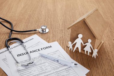 Sigorta formu yakından görmek, sigorta sağlık talep formu, kalem, stetoskop, ev modeli ve aile üzerinde ahşap masa kesilmiş kağıt