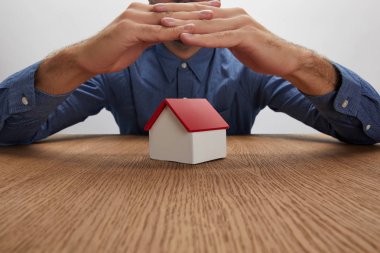 cropped shot of man holding hands above house model, insurance concept clipart