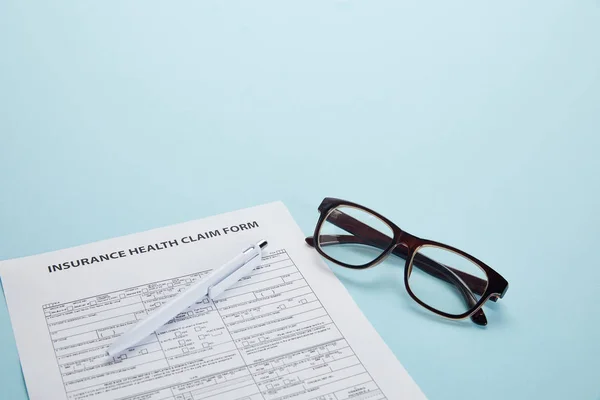 close-up view of insurance health claim form, pen and eyeglasses on blue