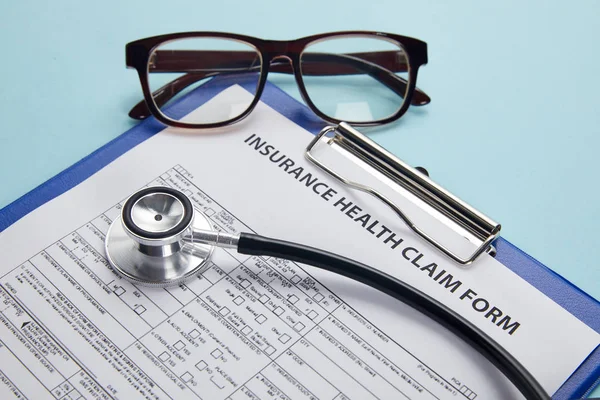insurance health claim form, clipboard, eyeglasses and stethoscope on blue