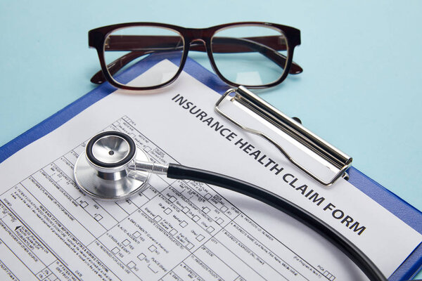 insurance health claim form, clipboard, eyeglasses and stethoscope on blue 