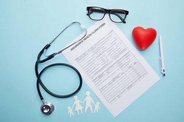 top view of insurance health claim form, eyeglasses, paper cut family, red heart symbol and stethoscope on blue  clipart
