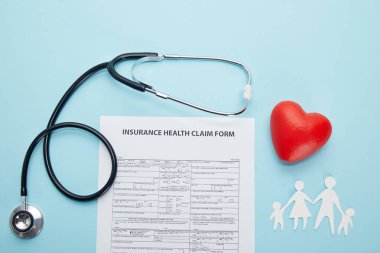 top view of insurance health claim form, paper cut family, red heart symbol and stethoscope on blue  clipart