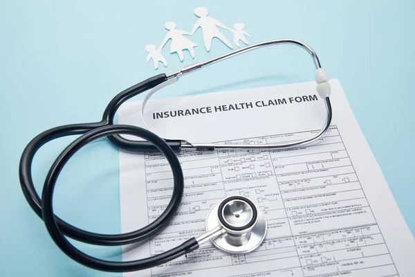 close-up view of insurance health claim form, paper cut family and stethoscope on blue