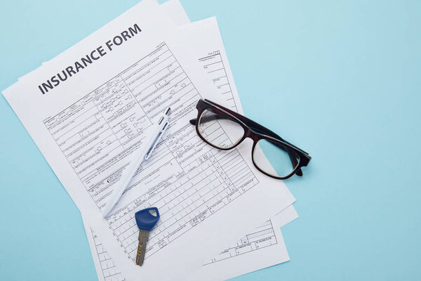 top view of insurance form, eyeglasses, key and pen isolated on blue 