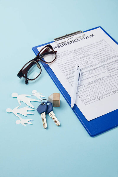 close-up view of insurance form, pen, paper cut family and keys isolated on blue   