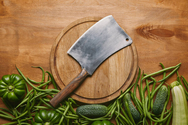 Metal cleaver on cutting board with green vegetables on wooden table