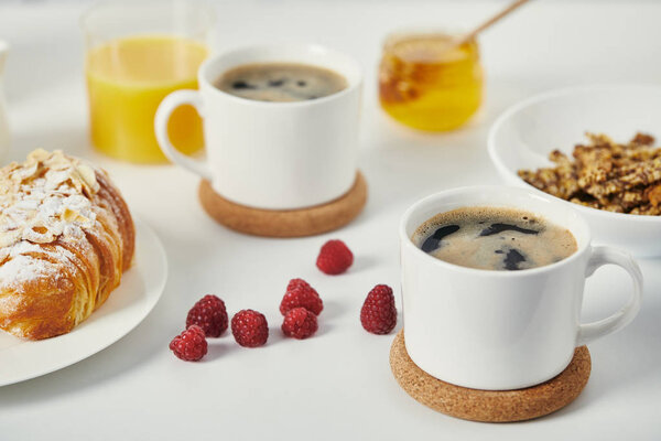 close up view of tasty breakfast with cups of coffee and croissant on white surface