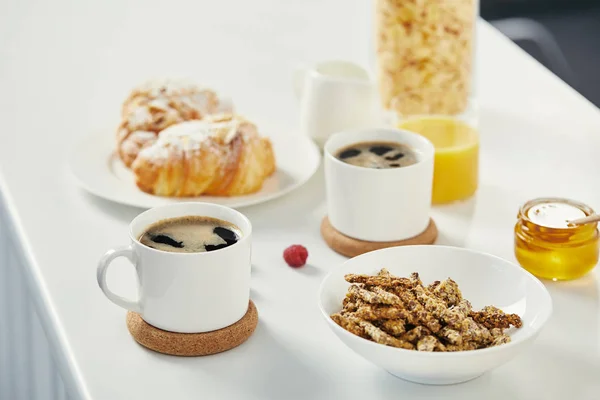 close up view of cups of coffee, honey and croissants for breakfast on white surface