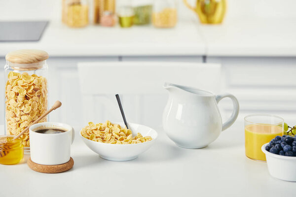 close up view of corn flakes in bowl, honey and cup of coffee for breakfast on white surface