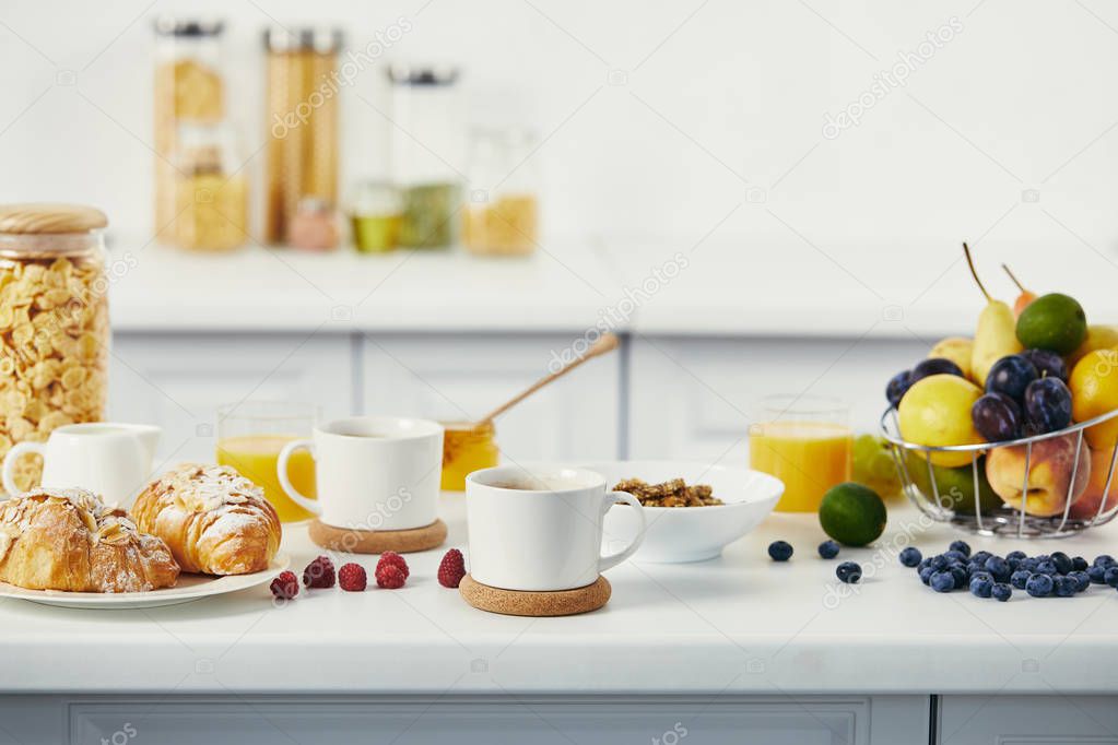close up view of cups of coffee and croissants for breakfast on white tabletop in kitchen