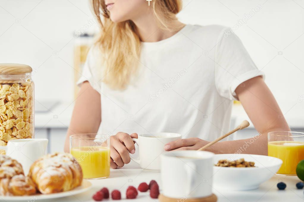 partial view of woman sitting at table with croissants, cups of coffee and glasses of juice for breakfast