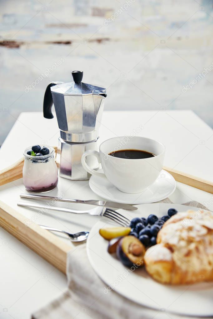 close up view of tasty breakfast with yogurt and cup of coffee on wooden tray on white surface