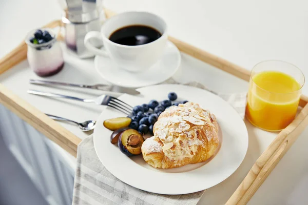 クロワッサン 新鮮なブルーベリーと梅ジュースのグラス コーヒーと白いテーブルの上の木製のトレイの朝食のヨーグルトのクローズ アップ表示 — ストック写真