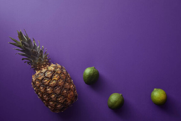 top view of pineapple and limes on violet surface