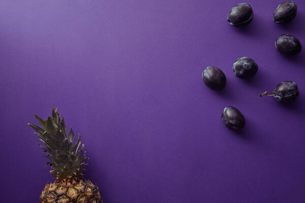 вид сверху на ананас и сливы на фиолетовую поверхность
