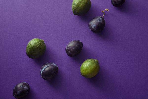 top view of plums and limes on violet surface