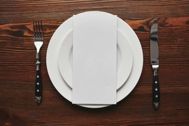 top view of blank card on white plates with fork and knife on wooden table 