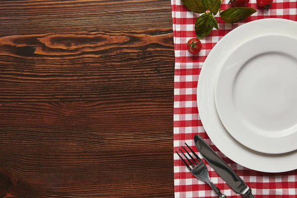 木の表面に空の白い皿 カトラリー トマトとバジルのトップ ビュー — ストック写真
