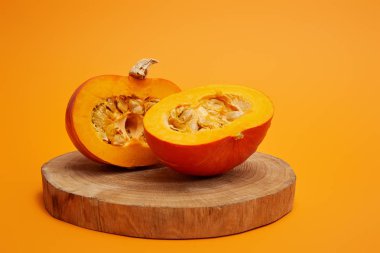 close-up view of ripe sliced pumpkin on round wooden board on orange background    clipart
