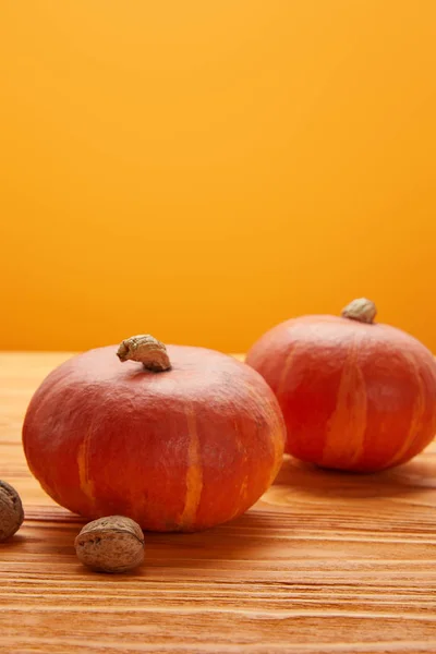 Vista Cerca Calabazas Maduras Nueces Superficie Madera Sobre Fondo Naranja —  Fotos de Stock