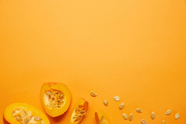 top view of raw ripe sliced pumpkin with seeds on orange background  