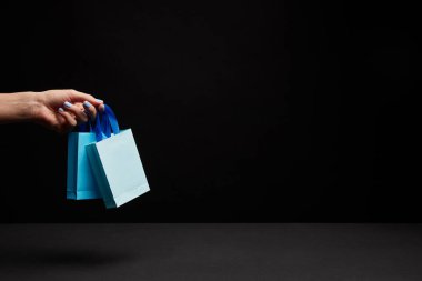 partial view of woman holding blue paper shopping bags on black background
