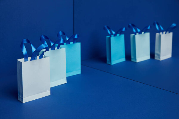 close up view of arranged paper shopping bags with mirror reflection on blue background